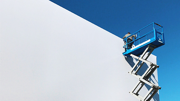 A person on a ladder painting a wall